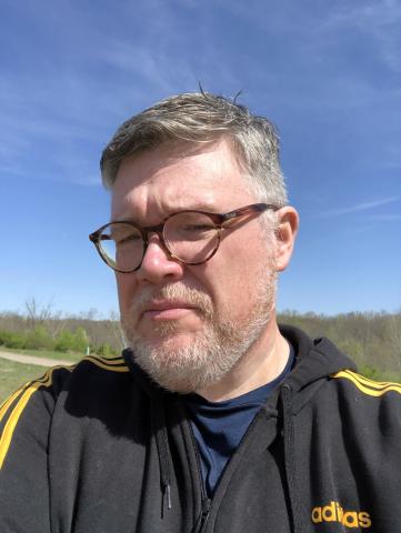 John, under a sky blue sky, admiring his post-quarantine hair cut.